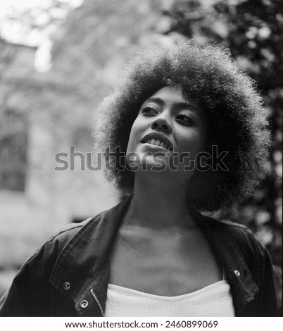 Film portrait of curly woman outdoors looking away. She is wearing a jacket and a white top. Image made with an analog medium format camera.