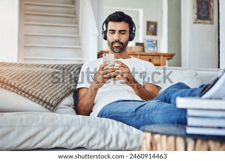 Man, phone and video with headphones on sofa for sound, audio and streaming service in living room with relax. Person, smartphone and mobile app for listening to music, radio and subscription in home