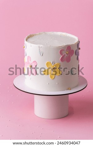 Beautiful spring cake for a girl or woman with white chocolate frosting decorated with colorful cream flowers. Pink background