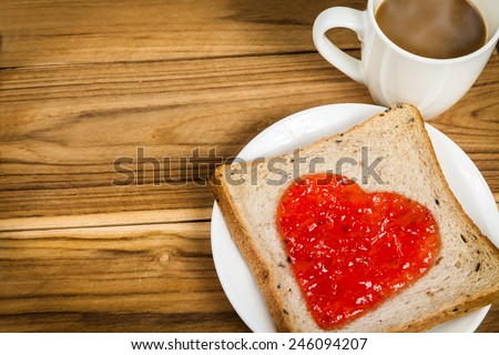 Delicious slice of bread with strawberry jam heart-shape and cup of coffee on wooden background for a Valentine's day, love concept, colorized vintage picture style