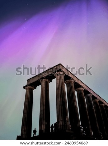 Stunning Aurora Borealis over Edinburgh's iconic National Monument on Calton Hill. Vibrant purple and pink hues dance across the night sky, illuminating the Greek-style columns.