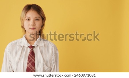 Close-up, young woman dressed in shirt stands and looks at the camera camera isolated on yellow background in studio