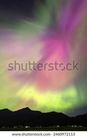 A vibrant aurora borealis dances in the night sky, displaying a mesmerizing blend of green, purple, and pink hues above a dark silhouette of a mountainous landscape