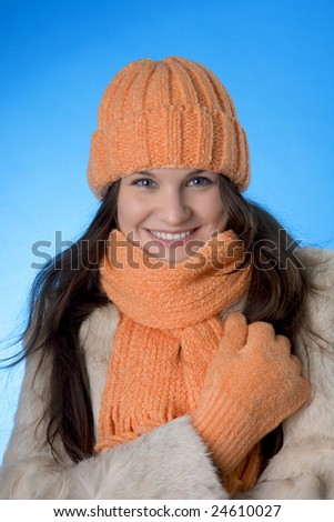 Picture of a beautiful brunette girl in the orange cap and coat on a blue background