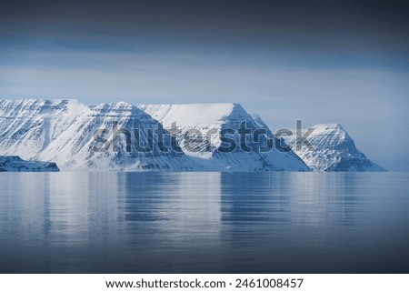 Iceland. Serene view of snow-covered mountains reflected on lake. Mountains are covered in snow and ice. Water is calm and still, providing peaceful atmosphere