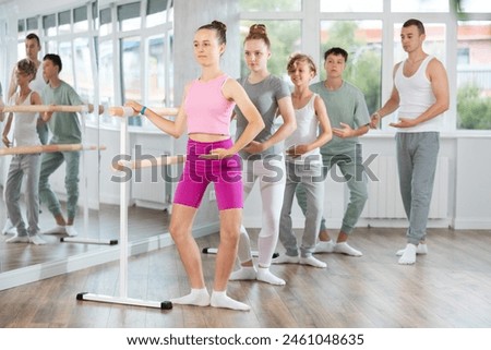 Slender teenage girl practicing plie position of ballet holding by ballet barre during choreography classes