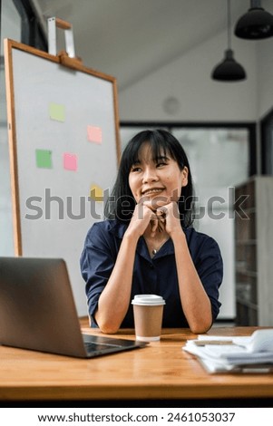 Cheerful young businesswoman with a warm smile sitting at her desk in a casual office environment with a coffee cup.