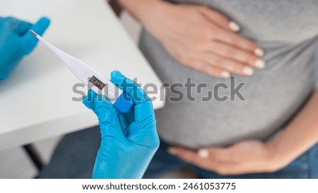 Pregnant woman with fever at doctor's appointment. Therapist holds an electronic thermometer with a temperature of 37.5. 