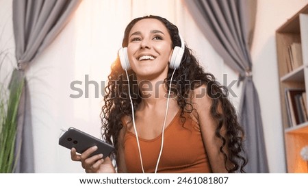 Music app. Sound inspiration. Amused smiling girl in headphones enjoying listening to song on phone at light home interior with free space. Royalty-Free Stock Photo #2461081807
