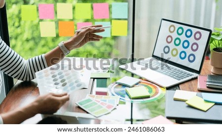 Creative graphic designer holding color swatch and comparing color on laptop for designing project.