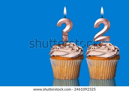 Birthday Cupcakes with Lit Question Mark Candle and Number 2 - Photo on Blue Background.