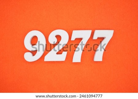 The number 9277 is made from white painted wood placed on a background of orange paper.