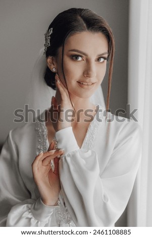 A woman in a white gown is posing for a picture. She has her hand on her face and is smiling. Concept of elegance and sophistication, as the woman is dressed in a wedding gown