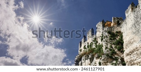 Moss and grass-covered battlements of a crumbling historic fortification, backlit against the radiant sun Royalty-Free Stock Photo #2461127901