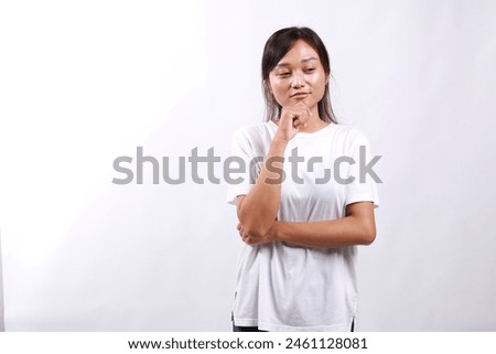 Sad, confused and bored young asian woman, looking at lower right corner with lonely and upset expression, standing over white background