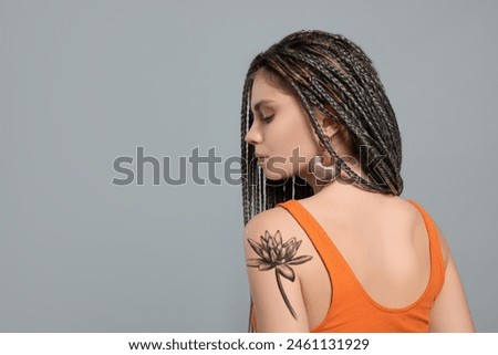 Young woman with tattoo of beautiful lotus flower on light grey background, space for text