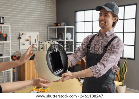 Male worker giving repaired coffee machine to client in workshop
