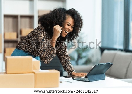 A young African American woman with afro brown hair works in a modern office, managing her online clothing store and live stream platform, sme box packages.