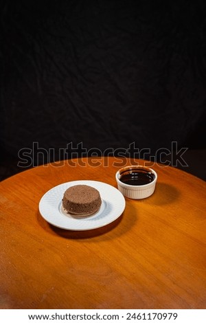 Chocolate brownies on a white plate and chocolate sauce in a cup, placed on a wooden table, black background, product photography To promote sales, dessert menus, coffee shops