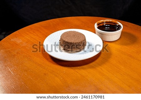 Chocolate brownies on a white plate and chocolate sauce in a cup, placed on a wooden table, black background, product photography To promote sales, dessert menus, coffee shops