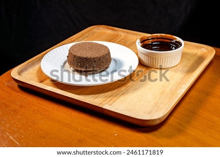 Chocolate brownies on a white plate and chocolate sauce in a cup Set and served on a wooden tray, placed on a wooden table, black backdrop, product photography To promote sales, dessert menus, coffee 