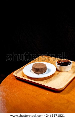 Chocolate brownies on a white plate and chocolate sauce in a cup Set and served on a wooden tray, placed on a wooden table, black backdrop, product photography To promote sales, dessert menus, coffee 
