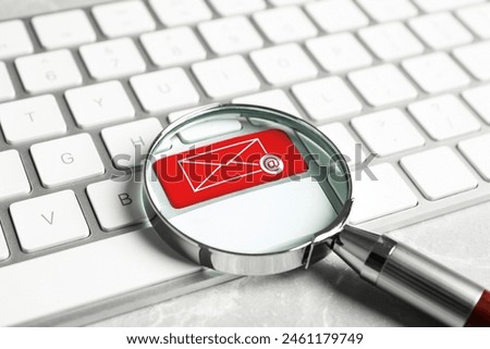 Red button with illustration of envelope and email sign on computer keyboard, view through magnifying glass