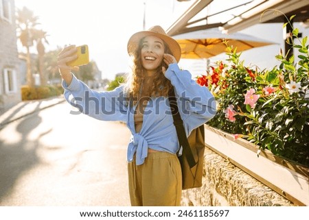 Young woman walks the streets and takes selfie using smartphone camera. Concept of positive moments, fun. Tourism and technology