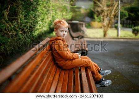The boy rests on a walk in the garden on a brown bench. Horizontal portrait of a red-haired Ukrainian