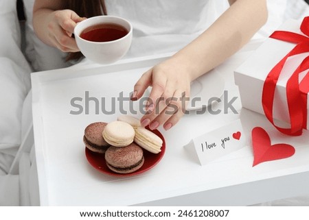 Tasty breakfast served in bed. Woman with tea, macarons, gift box and I Love You card at home, closeup
