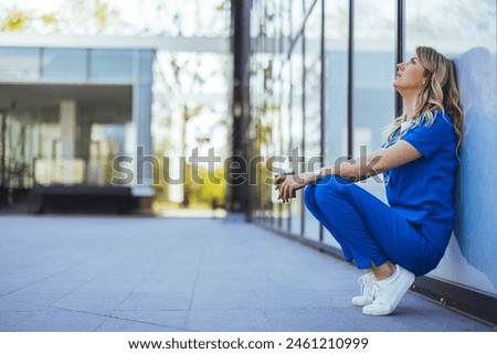 Tired nurse sits on floor outdoors of the medicine clinic after a hard dutty. Exhausted tired doctor or nurse. Clinic and hospital medical stuff working over hours. Overworked professional. 