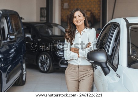Beautiful young saleswoman working at car showroom.  Professional confident sales person working in modern car dealership. Mature saleswoman at car dealership looking at camera.