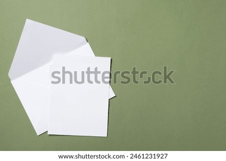 Letter envelope and card on green background, top view. Space for text