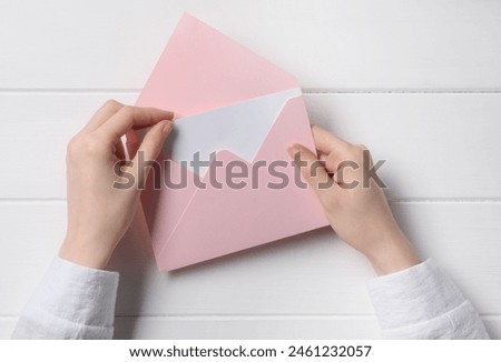 Woman taking card out of letter envelope at white wooden table, top view