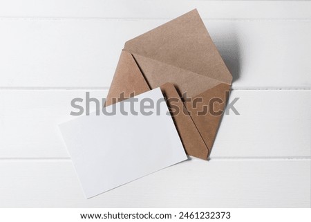 Blank sheet of paper and letter envelope on white wooden table, top view. Space for text