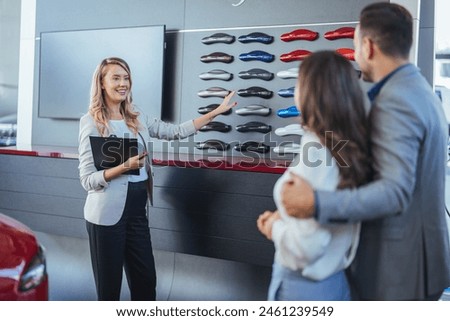 Young couple buying a car. Salesperson offering help to a couple in choosing a right color for their new car in a car salon. Car salesman making a sale.