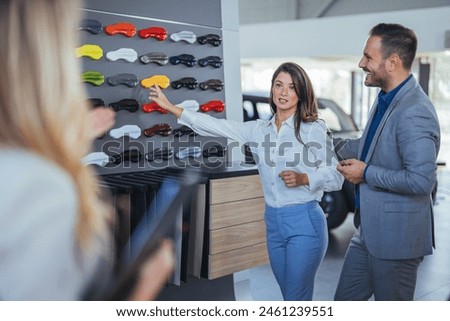 Salesperson offering help to a couple in choosing a right color for their new car in a car salon. Car sales business. Manager talking to couple, showing them new auto at dealership shop