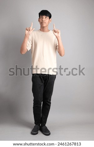 The Young South Asian teen with the casual clothes standing on the gray background, with gesture of pointing