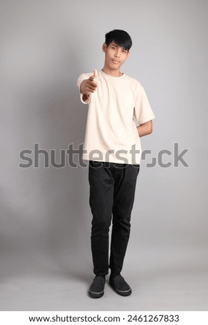 The Young South Asian teen with the casual clothes standing on the gray background, with gesture of pointing