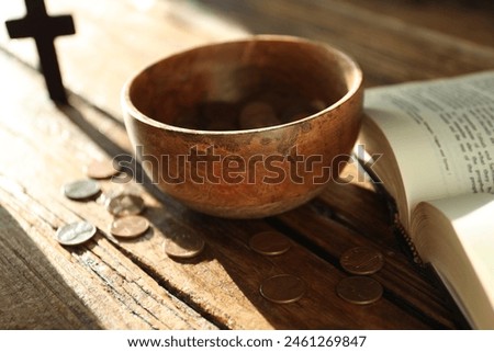 Donate and give concept. Bowl with coins, cross and Bible on wooden table in sunlights, selective focus