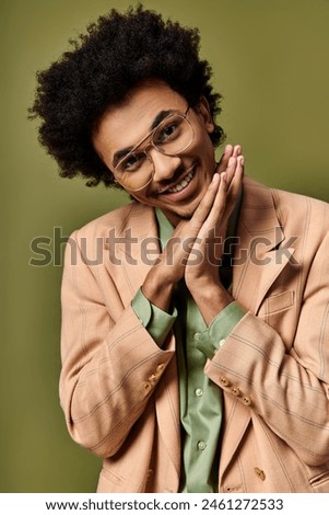 A stylish young African American man in a suit posing confidently for a picture against a green background.