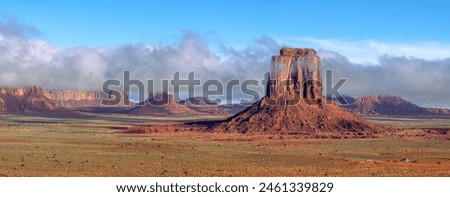 Low rainclouds hug a butte in Monument Valley's Navajo Tribal Park as rain hydrates the dry desert terrain at John Fords Point. Royalty-Free Stock Photo #2461339829