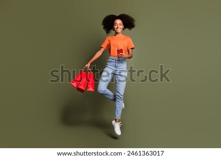 Full length photo of shiny attractive lady dressed orange outfit jumping typing device holding bargains isolated khaki color background