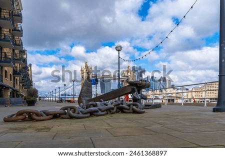 Large iron anchor with its chain belonging to a ship acting as a sculpture on the River Thames promenade with the Tower Bridge and the London skyline in the background. United Kingdom.