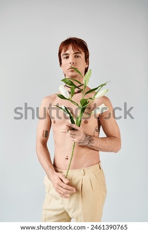 A shirtless young man gracefully cradles a plant in his hand, exuding a sense of peace and connection with nature.