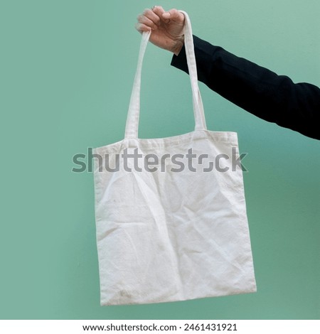 Woman in classic black blazer holding tote canvas blank eco bag on street green minimal wall background. Female consumer hold white textile shopper. template or place for your design, logo or text