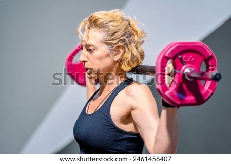 A woman is lifting a pink weight barbell. She is smiling and she is enjoying her workout. Fitness concept.