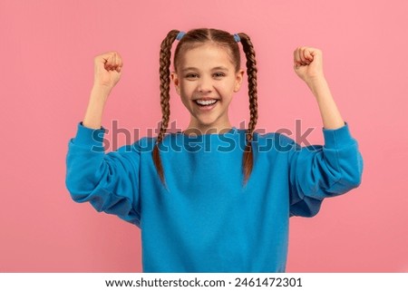 A cheerful young girl with braided hair is raising her fists in the air in a gesture of triumph or excitement, her joyful expression conveys a sense of victory or celebration