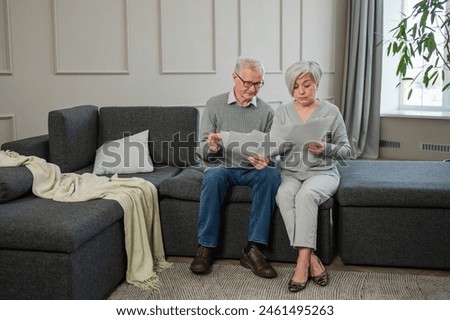 Sad tired disappointed middle aged senior couple sit with paper document. Unhappy older mature man woman reading paper bill managing bank finances calculating taxes planning loan debt pension payment Royalty-Free Stock Photo #2461495263