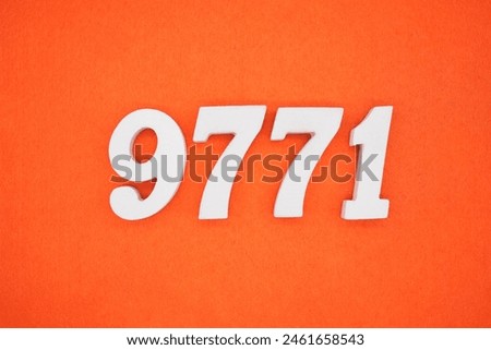The number 9771 is made from white painted wood placed on a background of orange paper.